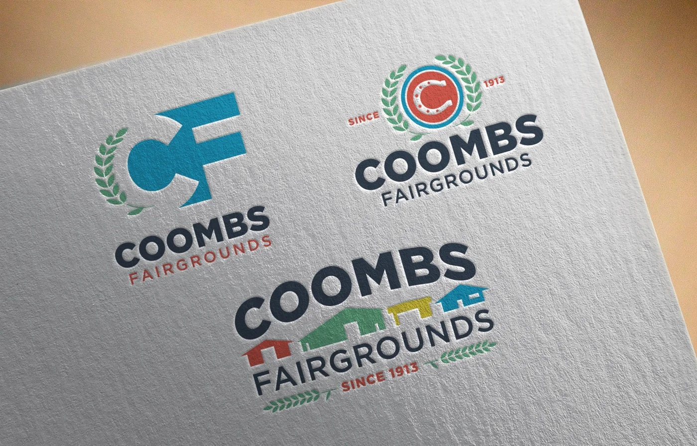 All three Coombs direction concepts debossed into cream letterpress paper: the Positive-Space CF monogram in blue with green laurel at the top left, the Circle C horseshoe badge at the top right, and the Facilities direction with colorful fairground buildings between COOMBS and FAIRGROUNDS at the bottom