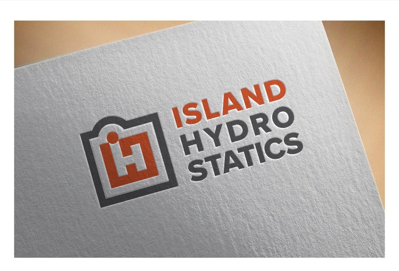 The iH Monogram concept applied to a letterpress mockup: a square badge containing a stylized iH letter combination in orange filling the badge interior with the negative space forming the letterforms, ISLAND HYDRO STATICS stacked in a heavy sans serif to the right
