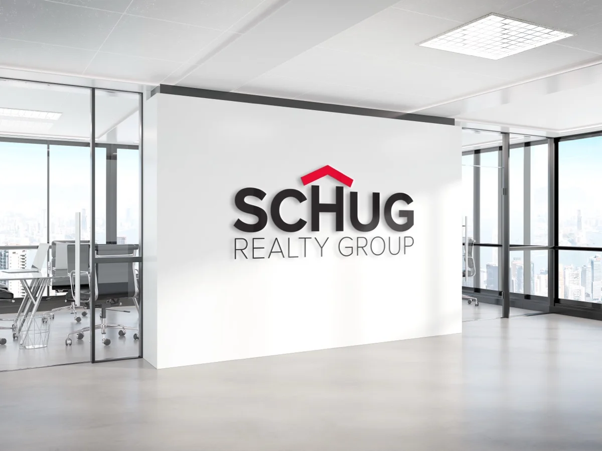 The Schug Realty Group logo applied as a dimensional black-and-red wall sign in a modern office interior with floor-to-ceiling windows