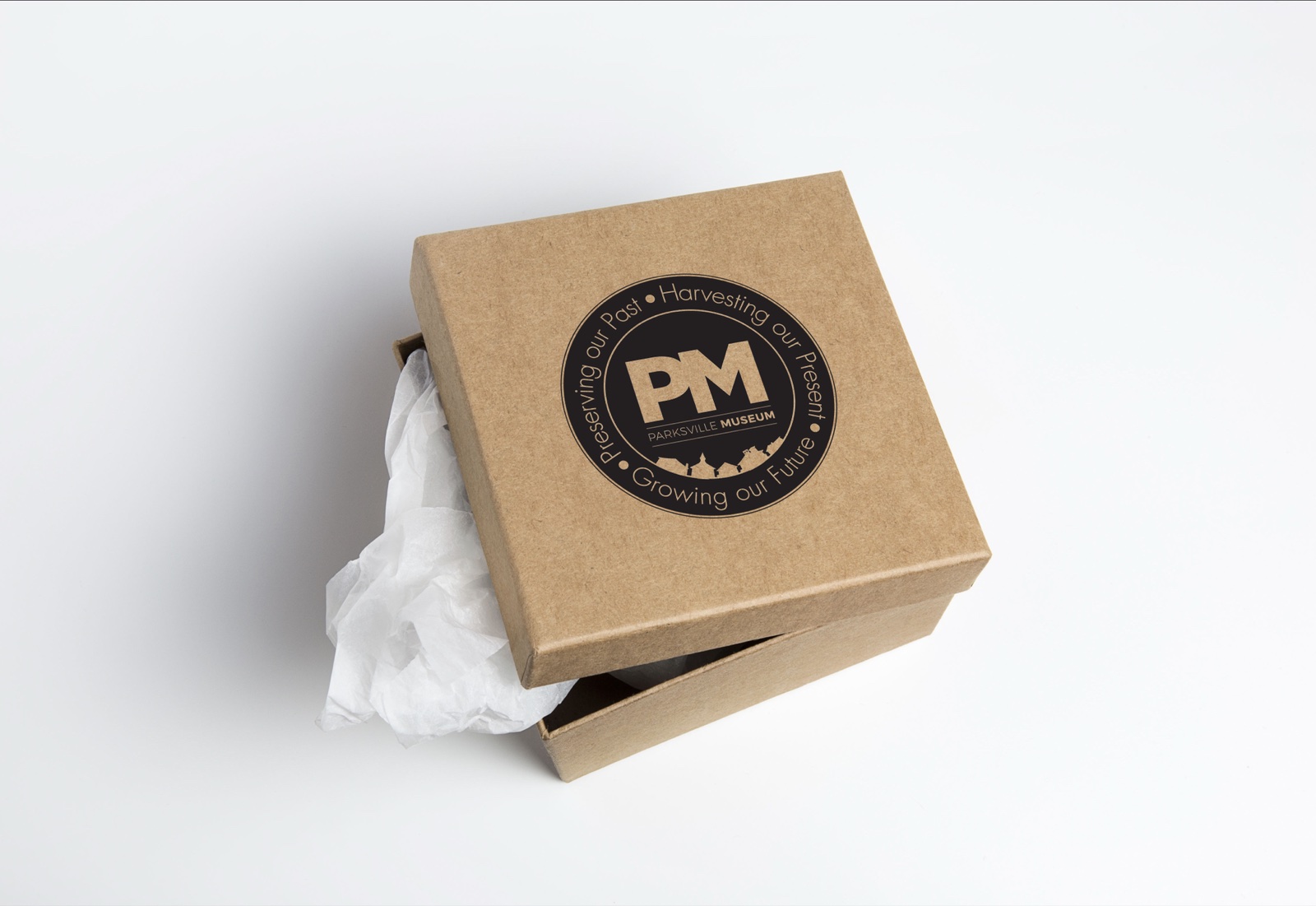 A kraft gift box with a circular PM monogram seal showing the Parksville Museum tagline around the edge