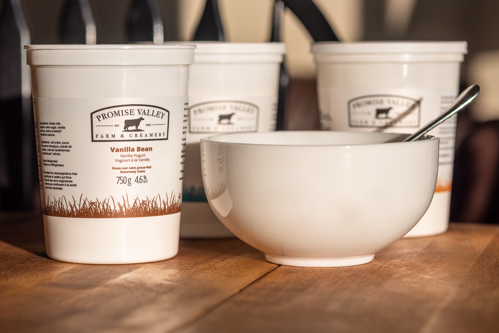 Promise Valley Farm yogurt containers alongside a white bowl with a spoon, suggesting the product being served
